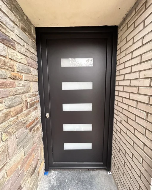 Porte d’entrée foncée avec quatre vitrages horizontaux dans une entrée en briques